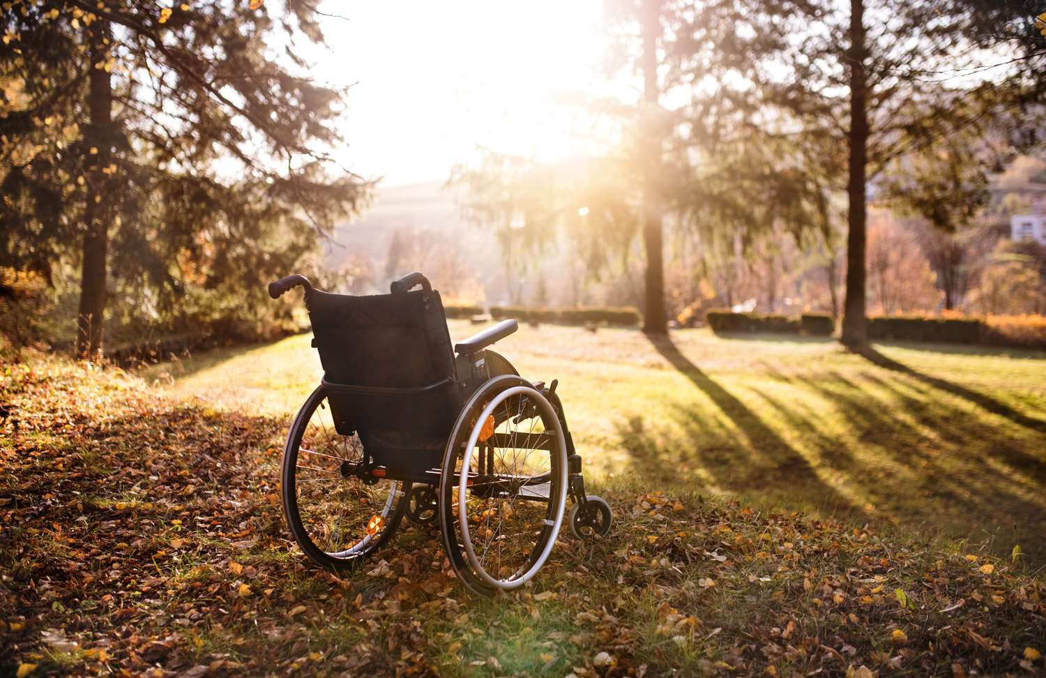 Empty wheelchair on a grass in park at sunset.